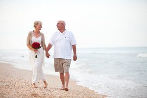 an older bride and groom walking hand in hand on the beach after renewing vows, renew wedding vow ideas, beach vow renewal