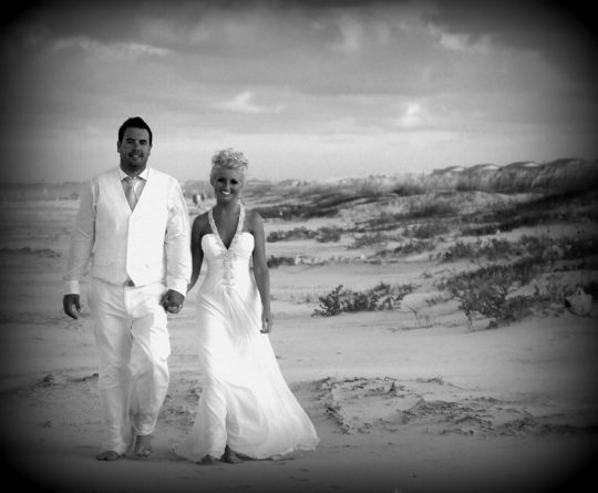 black and white photo of bride and groom walking on the beach