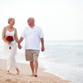 Older bride and groom walking along the beach