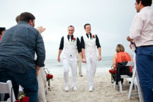 two gay men walking down the aisle in white suits and black shirts, gay marriage, same sex wedding