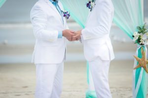 two gay men holding hands at the altar in white suits at a gay beach wedding, gay marriage, same sex wedding