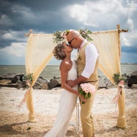 bride and groom kissing in front of beach wedding arbor