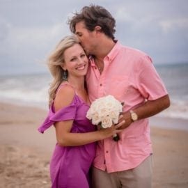 groom kissing bride on beach with bouquet