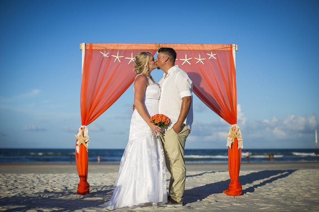 bride and groom in front of beach wedding arbor