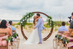 a bride and groom at the altar kissing in front of a boho arch, florida beach wedding, wedding planner