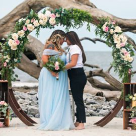 two wives with their foreheads touching in front of a boho altar, gay wedding, beach wedding