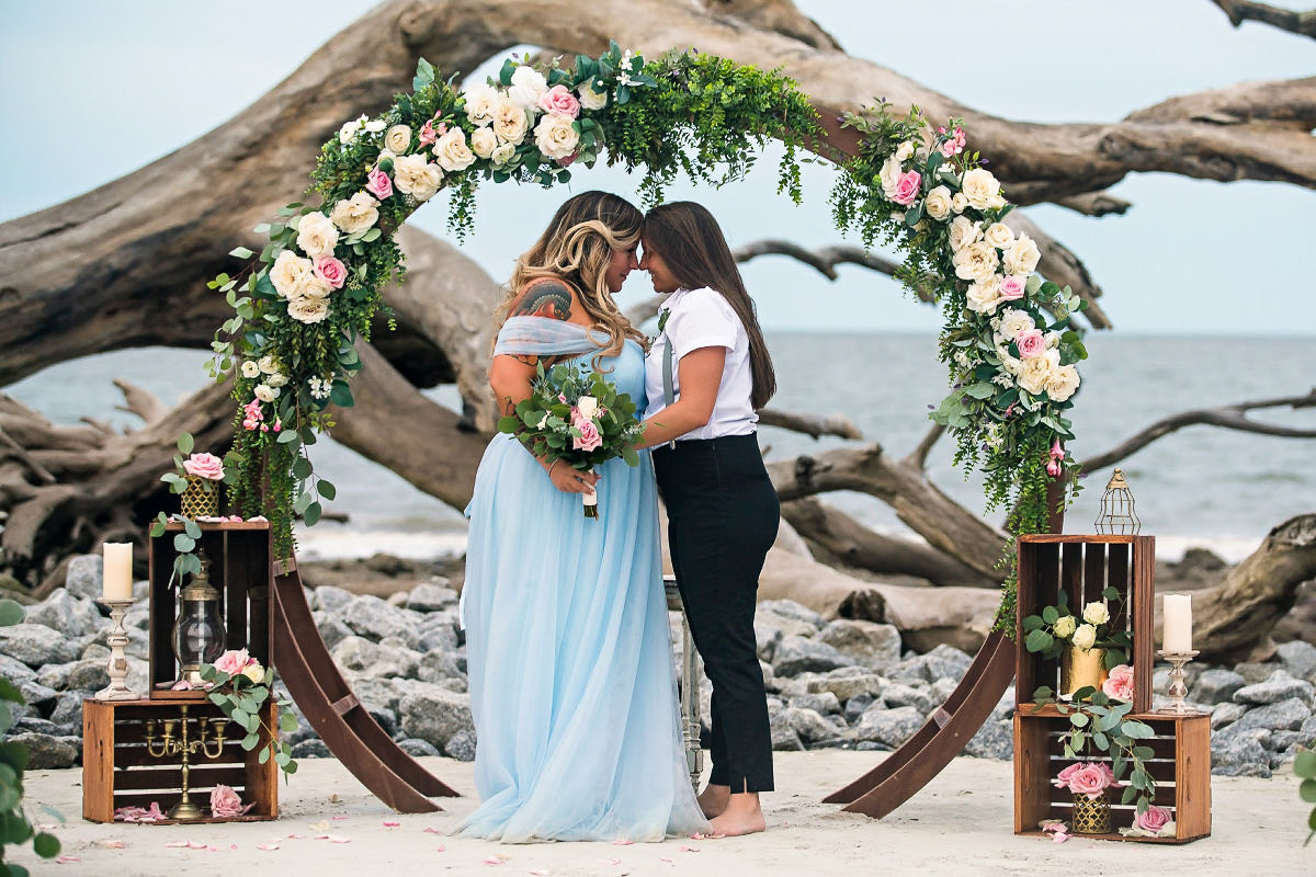 two wives with their foreheads touching in front of a boho altar, Same Sex Wedding, beach wedding attire