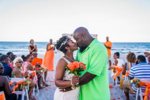 a bride and groom kissing each other with their guests in the background at their beach wedding, beach wedding attire, beach wedding planner
