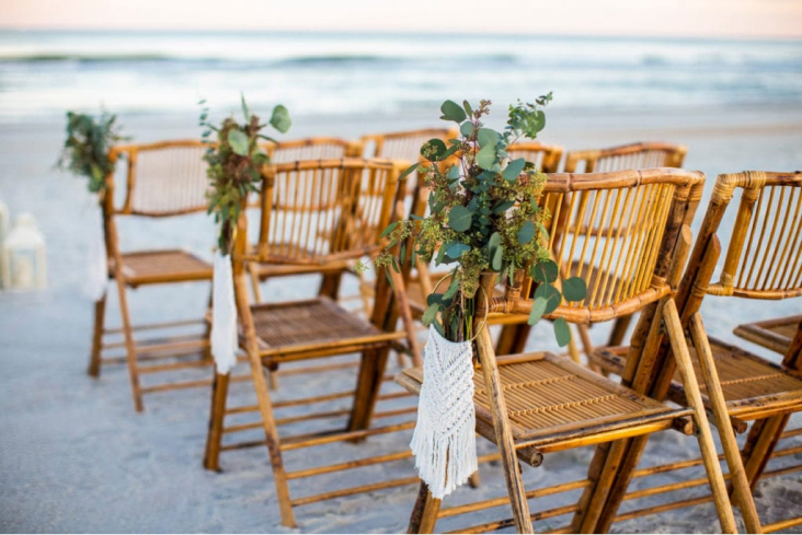 brown ceremony chairs with greenery on the beach