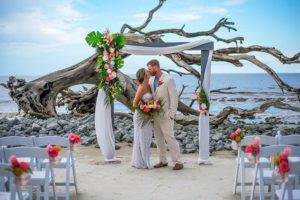 bride and groom kissing at tropical altar in front of rocky beachfront, beach music, best beach wedding planner, florida beach wedding
