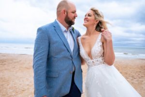 a bride and groom laughing and looking at each other while standing on the beach, beach wedding, beach wedding attire