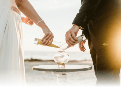 artistic shot of bride and groom pouring sand at beachfront altar