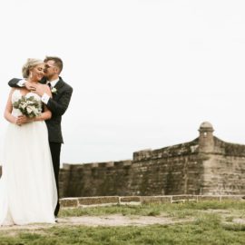 a groom hugging his bride from behind at castillo de san marcos in st augustine beach florida, luxury wedding venue florida, beach wedding venues florida