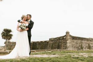 a groom hugging his bride from behind at castillo de san marcos in st augustine beach florida,  luxury wedding venue florida, beach wedding venues florida