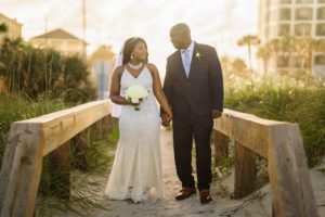 a black bride and groom standing on the walking deck out into the beach, beach wedding, beach wedding florida