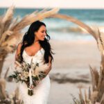 a new bride posing in front of a boho wedding arch on the beach in st augustine fl