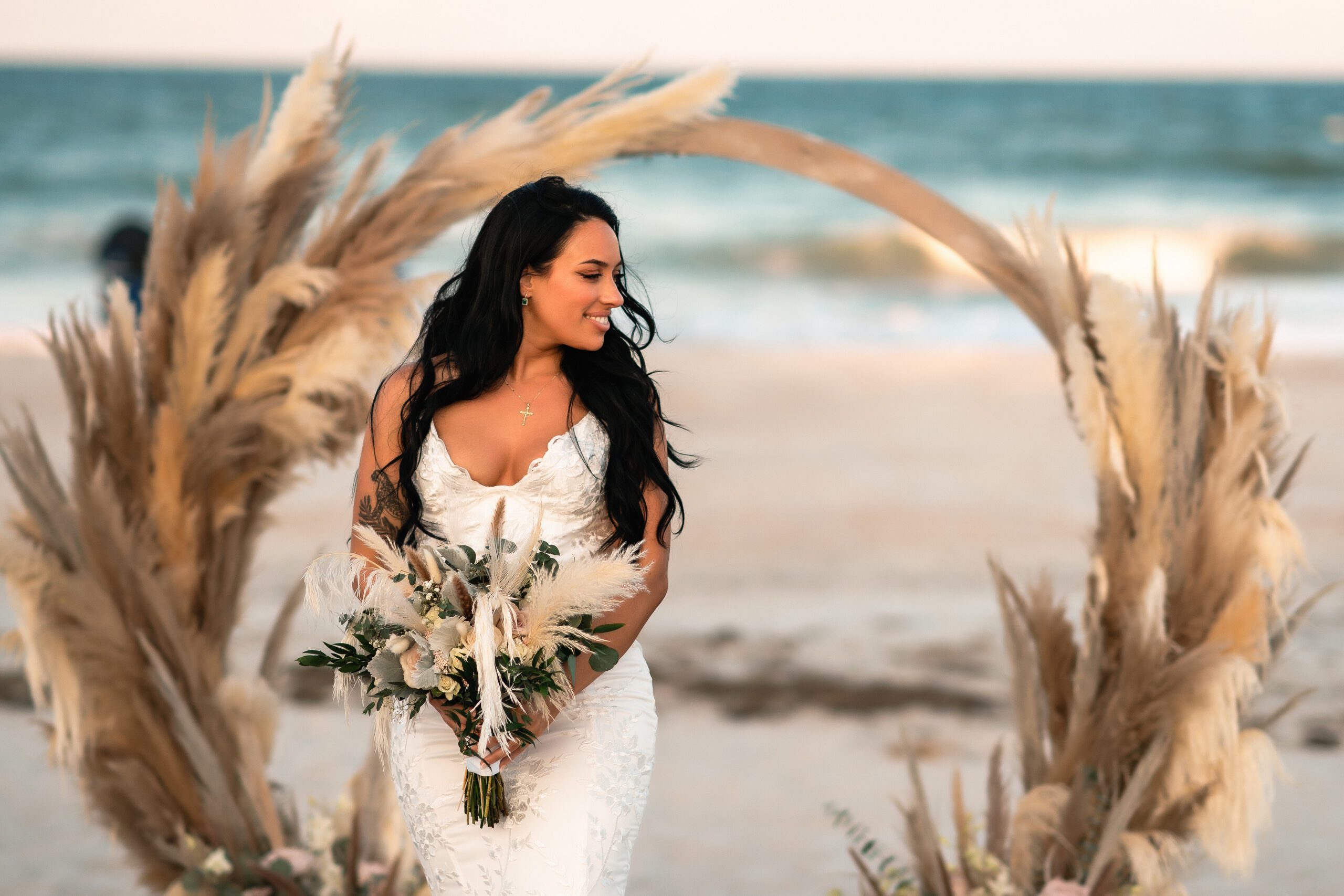 a new bride posing in front of a boho wedding arch on the beach in st augustine fl