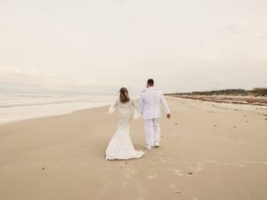 a married couple walking away from the camera on a cloudy day at the beach, beach wedding, winter beach wedding