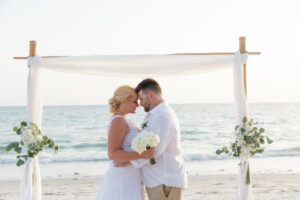 a bride and groom touching foreheads as they stand in front of the altar at a beach wedding, how to write wedding vows, wedding vows