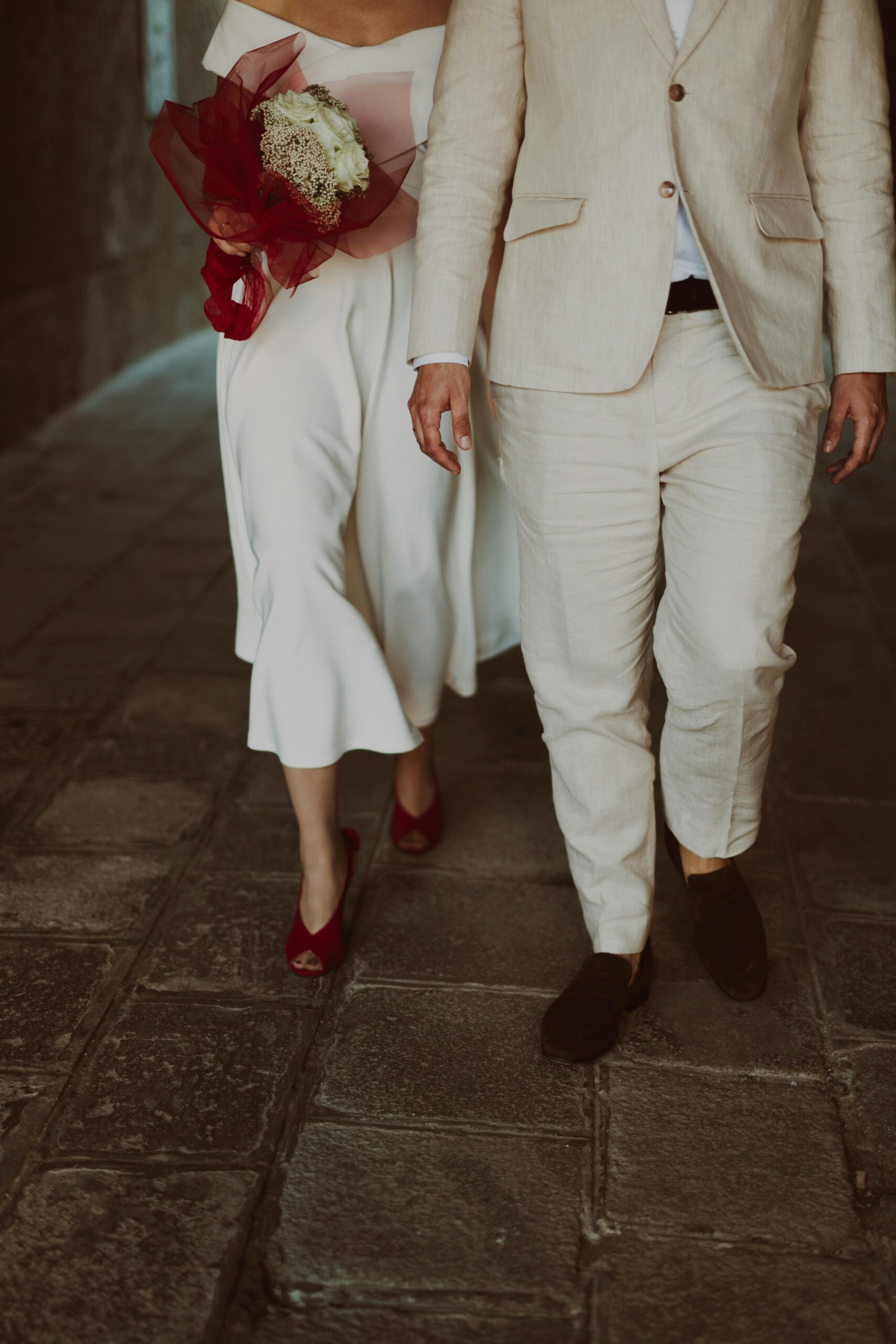 Bride and groom walking hand in hand at an outdoor summer wedding, wearing a linen suit and white gown — what to wear to an outdoor summer wedding.